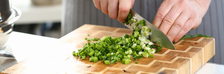 Wall Mural - Closeup of hands of cook holding knife for cutting green onions. Sliced fresh green onions and cooking vegetables in kitchen