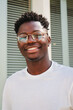 © Jose Calsina - Vertical portrait of one young african american teenager smiling and looking at camera standing outdoors. Front view of happy and joyful man with eyeglasses and white perfect teeth. Lyfestyle concept