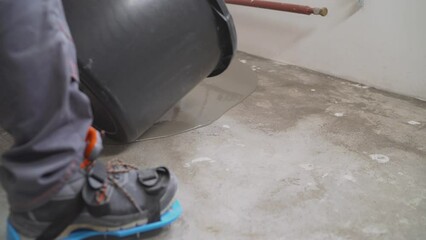 Poster - A male worker working with self-levelling cement mortar during a floor repair. A worker pours a bucket of mortar to level the floor. Self-levelling concrete floor mix.