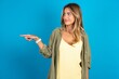 © Roquillo - young beautiful blonde woman standing over blue studio background points at copy space and advertises something, advices best price.
