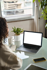 Over shoulder vertical view of girl student elearning looking at white mock up screen using laptop computer learning online, hybrid working at home office. Website mockup display template for ads.