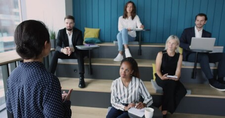 Wall Mural - Back view of business speaker woman talking to multiethnic corporate audience, giving seminar, lecture to diverse team of listening colleagues, teaching, training employees for new skills