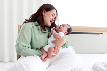 Mother holds infant newborn baby boy in arm and plays with him on bed in bedroom, lovely family mom and child stand time together, parent take care kid, overweight mom with fat body after childbirth.