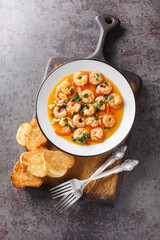 Wall Mural - Spanish Garlic Shrimp Gambas al Ajillo closeup on the plate served with toasts on the wooden board. Vertical top view from above