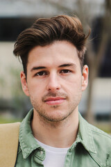 Wall Mural - Vertical close up portrait of confident teenage male student looking serious and relaxed at camera in a college. Handsome caucasian guy standing in university campus with pensive expression. High