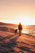 Frau und Hund gehen am Strand spazieren und erleben einen wunderschönen Sonnenuntergang am Meer 