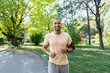 © Liubomir - Latin American cheerful and smiling running in the park man listening to music and audio podcasts, runner smiling and looking at the camera, joyful sportsman outdoors in the day.
