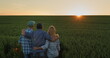 A friendly family of farmers admiring the sunset over a field of wheat