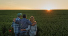 A Friendly Family Of Farmers Admiring The Sunset Over A Field Of Wheat