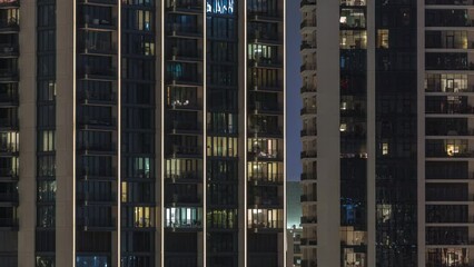 Wall Mural - Evening light in rooms in towers and skyscrapers. Tall blocks of flats with glowing windows located in residential district of city aerial timelapse.