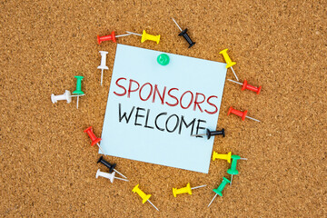 Poster - Sponsors welcome text on light blue post-it paper pinned on bulletin cork board surrounding by multi color pins. This message can be used in business concept about sponsors welcome.