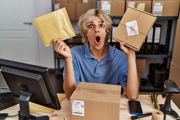 Canvas Print - Young man working at small business ecommerce holding packages afraid and shocked with surprise and amazed expression, fear and excited face.