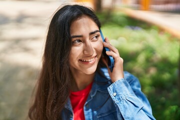 Wall Mural - Young hispanic girl smiling confident talking on the smartphone at park