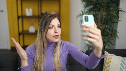 Poster - Young blonde woman having video call sitting on sofa at home