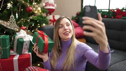 Poster - Young blonde woman make selfie by smartphone sitting on floor by christmas tree at home