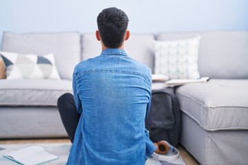 Wall Mural - Young hispanic man sitting on the floor studying for university standing backwards looking away with crossed arms