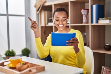 Sticker - African american woman using touchpad sitting on the table at breakfast smiling happy pointing with hand and finger to the side