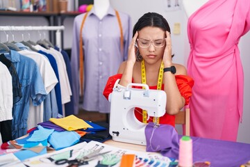 Poster - Hispanic young woman dressmaker designer using sewing machine with hand on head, headache because stress. suffering migraine.