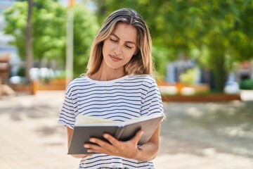 Canvas Print - Young blonde woman reading book at park