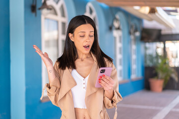 Poster - Young woman at outdoors looking at the camera while using the mobile with surprised expression