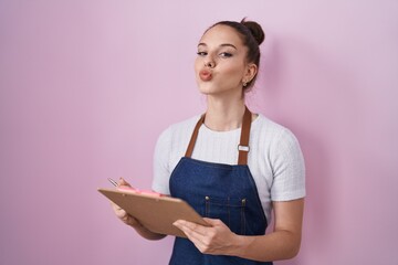 Poster - Young hispanic girl wearing professional waitress apron taking order looking at the camera blowing a kiss being lovely and sexy. love expression.