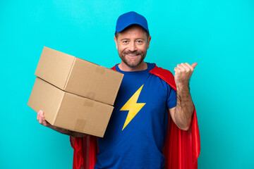 Wall Mural - Super Hero delivery man isolated on blue background pointing to the side to present a product