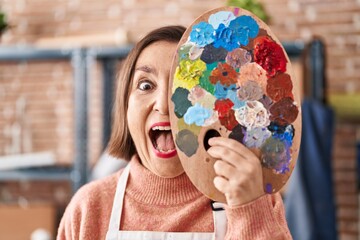 Wall Mural - Middle age hispanic woman holding painter palette close to face celebrating crazy and amazed for success with open eyes screaming excited.