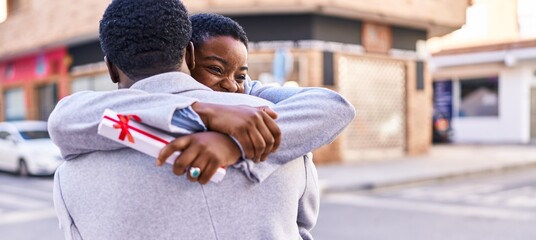 Wall Mural - Man and woman couple hugging each other surprise with gift at street