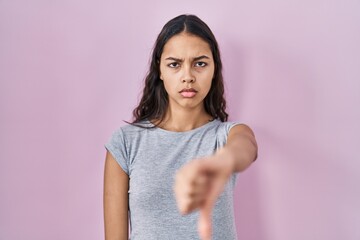 Wall Mural - Young brazilian woman wearing casual t shirt over pink background looking unhappy and angry showing rejection and negative with thumbs down gesture. bad expression.