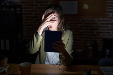 Poster - Blonde caucasian woman working at the office at night peeking in shock covering face and eyes with hand, looking through fingers with embarrassed expression.