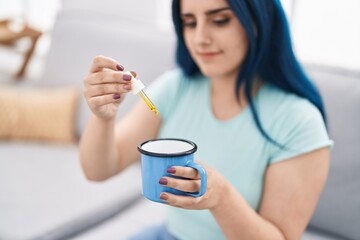 Poster - Young caucasian woman pouring liquid on cup sitting on sofa at home