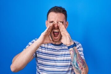 Poster - Young hispanic man standing over blue background shouting angry out loud with hands over mouth