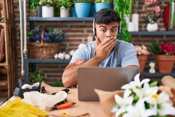 Poster - Hispanic young man working at florist shop doing video call covering mouth with hand, shocked and afraid for mistake. surprised expression