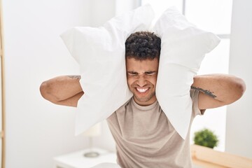 Wall Mural - African american man suffering for noise covering ears with pillow at bedroom