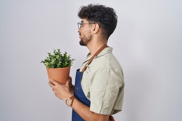 Wall Mural - Arab man with beard holding green plant pot looking to side, relax profile pose with natural face and confident smile.