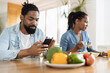 © Goran - Young African American man using smart phone while having breakfast with his girlfriend at dining table