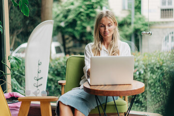 Wall Mural - Young woman freelancer works remotely while sitting in a modern coffee shop.