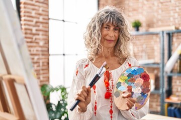 Canvas Print - Middle age woman artist smiling confident holding paintbrushes and palette at art studio