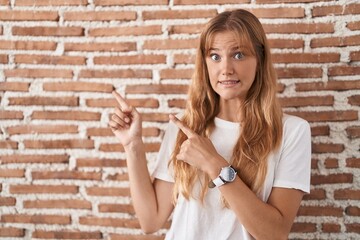 Sticker - Young caucasian woman standing over bricks wall pointing aside worried and nervous with both hands, concerned and surprised expression