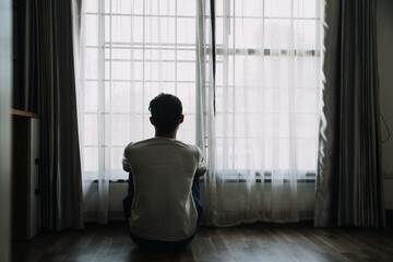 Alone man silhouette staring at the window closed with curtains in bedroom. Man stands at window alone