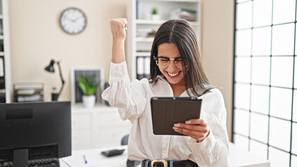 Young beautiful hispanic woman business worker using touchpad with winner expression at office