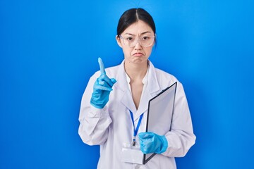 Canvas Print - Chinese young woman working at scientist laboratory pointing up looking sad and upset, indicating direction with fingers, unhappy and depressed.