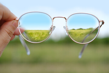 closeup woman checks gold-rimmed glasses, wheat field in lenses, cleanliness and transparency lenses