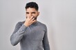 Hispanic man with beard standing over white background smelling something stinky and disgusting, intolerable smell, holding breath with fingers on nose. bad smell