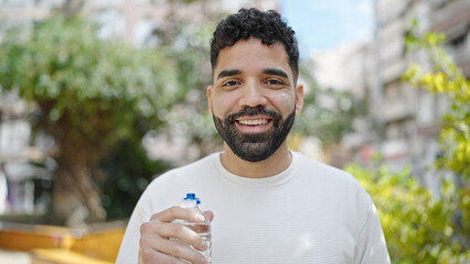 Sticker - Young hispanic man smiling confident holding bottle of water at park