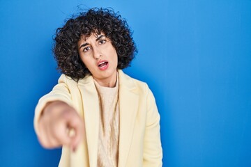 Canvas Print - Young brunette woman with curly hair standing over blue background pointing displeased and frustrated to the camera, angry and furious with you