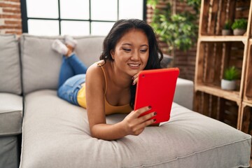 Poster - Young chinese woman using touchpad lying on sofa at home