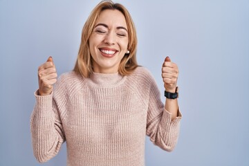 Canvas Print - Hispanic woman standing over blue background excited for success with arms raised and eyes closed celebrating victory smiling. winner concept.