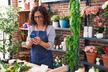 Wall Mural - Middle age woman florist smiling confident using smartphone at flower shop