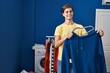 © Krakenimages.com - Young caucasian man smiling confident putting sweatshirt on hanger at laundry room